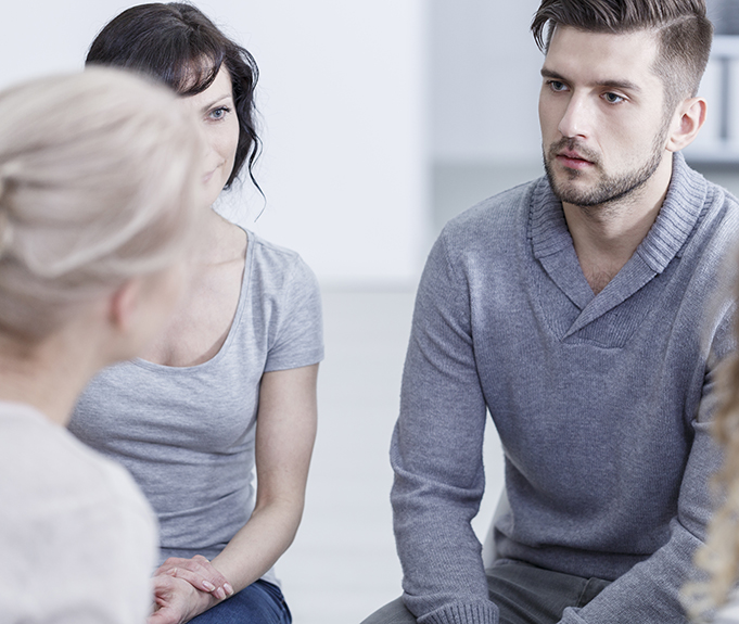 Unhappy young man sitting with other people during addiction therapy
