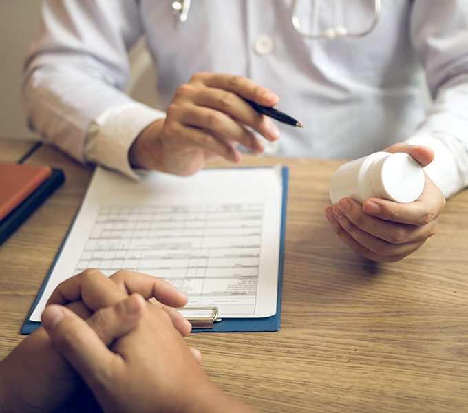 Confident doctor man holding a pill bottle and talking with senior patient and reviewing his medication at office room.