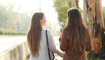 Back view portrait of two women walking and talking in a park asunny day