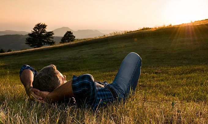 Mature man taking a break and relax in a meadow in the wonderful warm light of the sunset