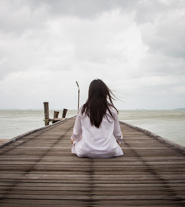 Meditation by young women in white dress on a bridge by the sea.