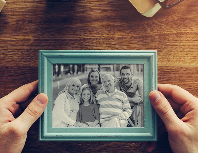 My family is my inspiration. Close-up top view of man holding photograph of his family over wooden desk with different chancellery stuff laying around